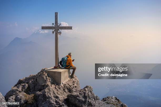 excursionista sentado en la cima de la montaña usando un teléfono inteligente - cruz objeto religioso fotografías e imágenes de stock