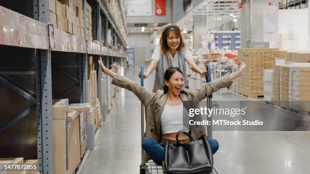 group of young asian women customer pushes shopping cart fun racing in trolley through in retail warehouse. business warehouse shopping. - shopping trolleys stockfoto's en -beelden