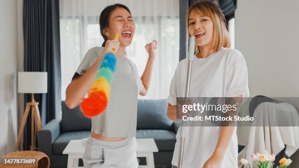 junge asiatische lesbische paare haben spaß beim putzen des hauses und singen mit wischmopp im wohnzimmer. tanzen und singen in einem gemütlichen raum. - mop stock-fotos und bilder