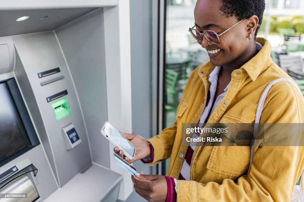 African American woman is withdrawing money at the outdoor ATM