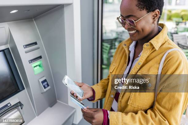 african american woman is withdrawing money at the outdoor atm - atm stock pictures, royalty-free photos & images