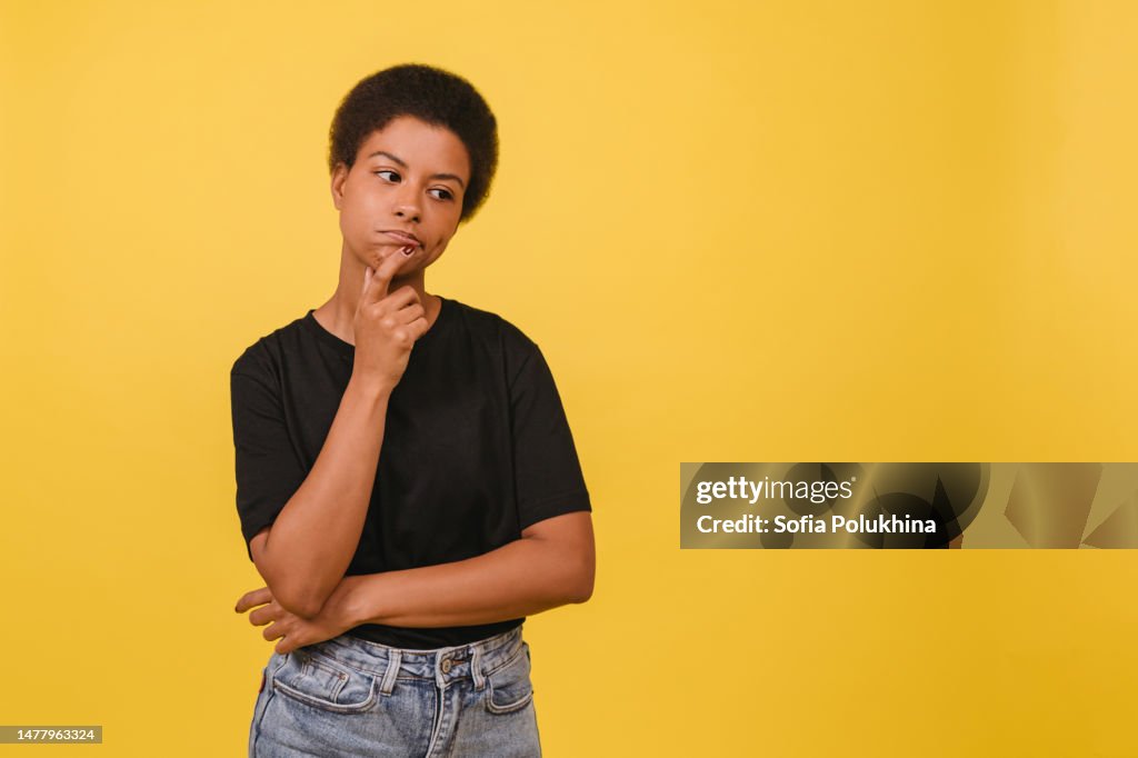 Portrait of thinking young black woman on yellow backdrop