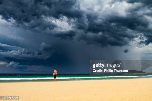 man standing on beach with dark dramatic storm cloud and rain coming - extreme weather events stock pictures, royalty-free photos & images