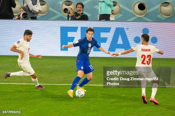 Brenden Aaronson of the United States attempts to dribble past Karim Ansarifard of Iran and Ramin Rezaeian of Iran during a game between Iran and...