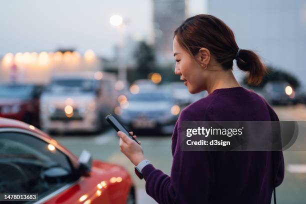 young asian businesswoman using smartphone while walking to her car, commuting in the city, with urban cityscape in background. business on the go concept - vehicle key photos et images de collection