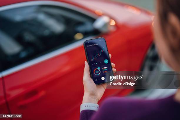 young asian businesswoman checking her financial and investment data with online banking account on smartphone, standing by her car in the city. managing personal banking and financial service at easy access. financial planning. wealth management concept - red billed stock pictures, royalty-free photos & images