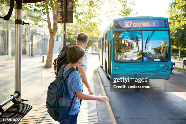 man and young son standing at bus stop as vehicle approaches - approaching imagens e fotografias de stock