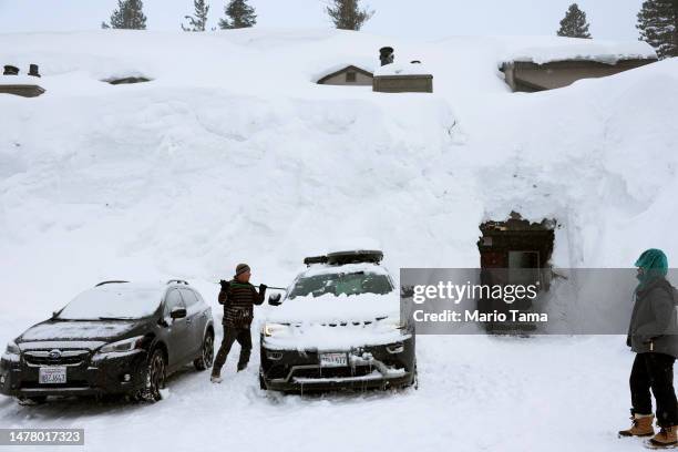 Person removes snow in front of lodging obscured by snowbanks piled up from new and past storms in the Sierra Nevada mountains, after yet another...