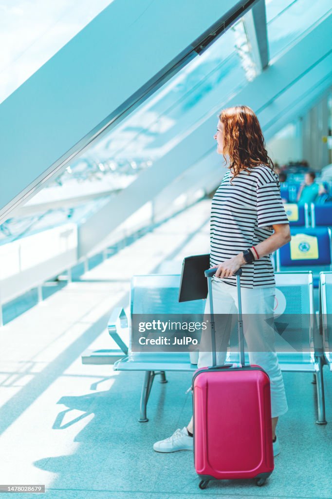 Young adult woman with laptop and suitcase at the airport waiting for her flight