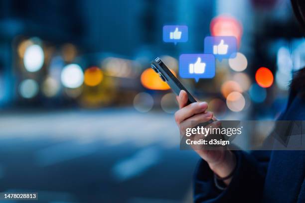 close up of a young woman using smartphone on social media network application. viewing posts, giving likes or love, making friends on social media pages in the city. people engaging in networking with technology. social media addiction concept - facebook stock-fotos und bilder