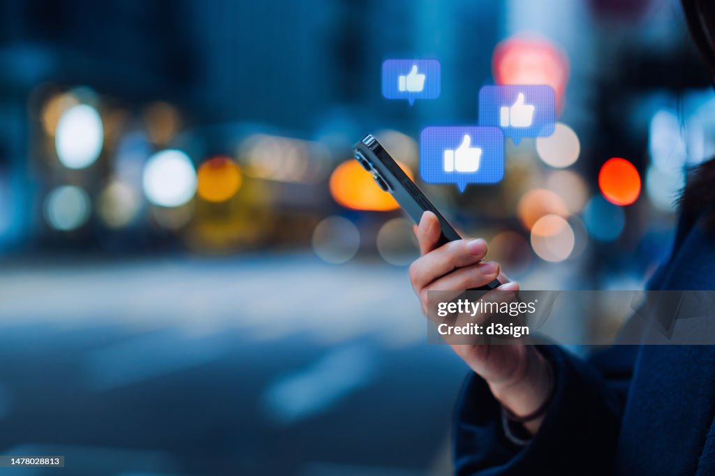 Close up of a young woman using smartphone on social media network application. Viewing posts, giving likes or love, making friends on social media pages in the city. People engaging in networking with technology. Social media addiction concept