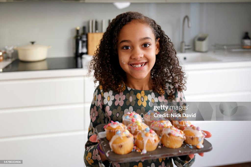 Portrait of a smiling young girl with a tray of freshly decorated cakes