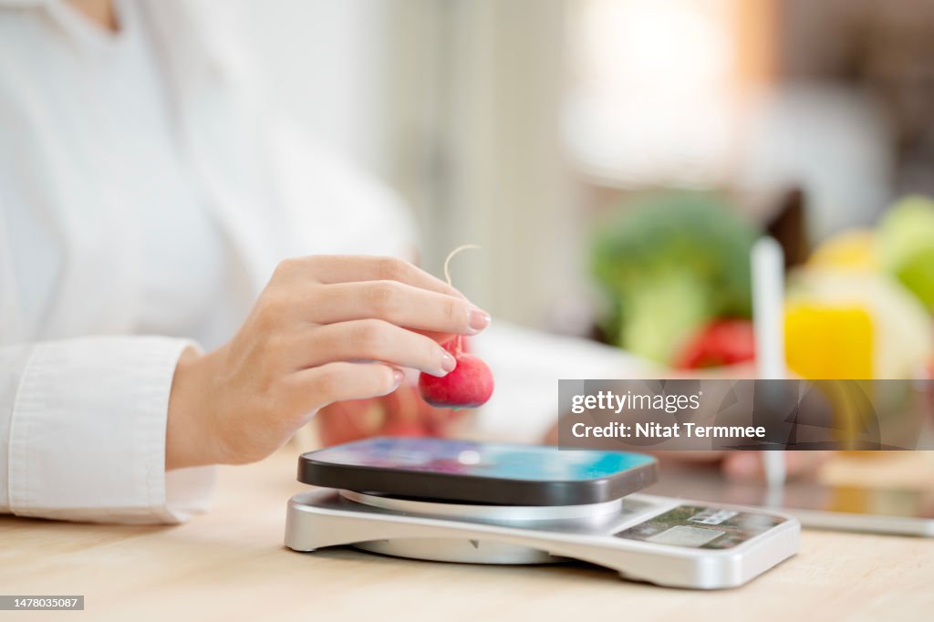 Radish is a Power Source of Potassium, Vitamin C, and Fiber. Close-up shot of female nutritionists weighing radishes on digital scales during doing a nutrition plan and inputting data on a tablet computer.