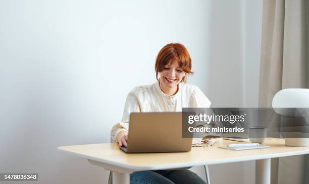 smiling young woman studying online on a laptop computer at home - mid volwassen vrouw stockfoto's en -beelden