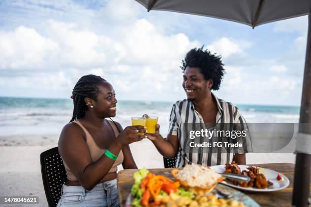 pareja de adultos medianos haciendo un brindis de celebración en un restaurante en la playa - black couple honeymoon fotografías e imágenes de stock