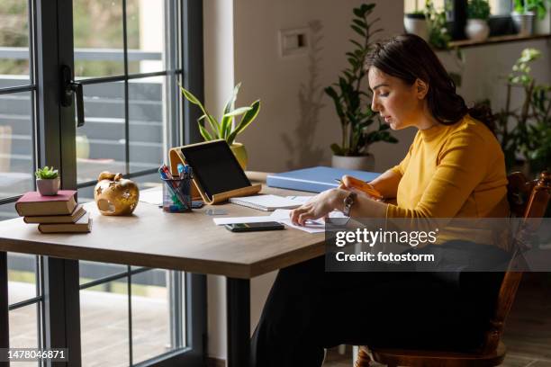 young woman sorting out her bills and finances at home office desk - yellow note pad stock pictures, royalty-free photos & images