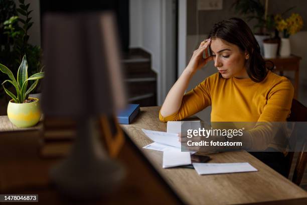 young woman sorting out her monthly bills and struggling with finances - yellow note pad stock pictures, royalty-free photos & images