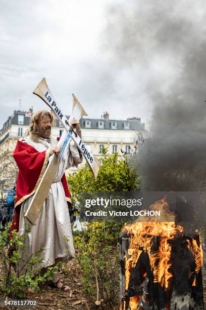 Feu de poubelle et homme déguisé en Jésus Christ tenant une croix chrétienne avec l'inscription "La Paix, l'épée" lors de la manifestation contre la...