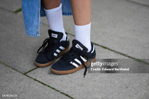 Gabriella Berdugo wears a blue asymmetric half long and half short skirt, white socks, black suede and white logo pattern sneakers from Adidas,...