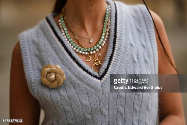 Gabriella Berdugo wears a silver pearls necklace, a green stones necklace, gold chains necklaces, a blue with black and white borders strap print...