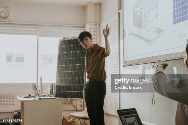 grouping design work project, master's degree student helping present their solar panel system work in front of class. - green economy stockfoto's en -beelden