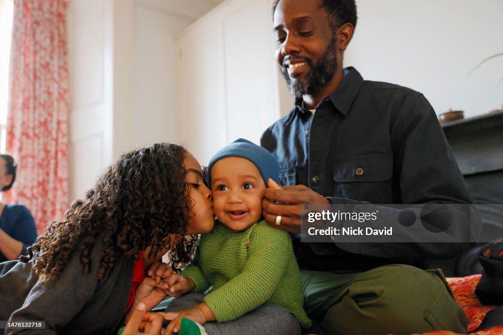 A father helps get his baby son dressed putting on his hat