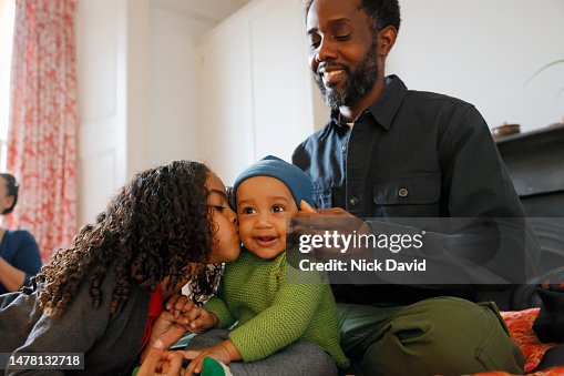 A father helps get his baby son dressed putting on his hat A father helps get his baby son dressed putting on his hat
