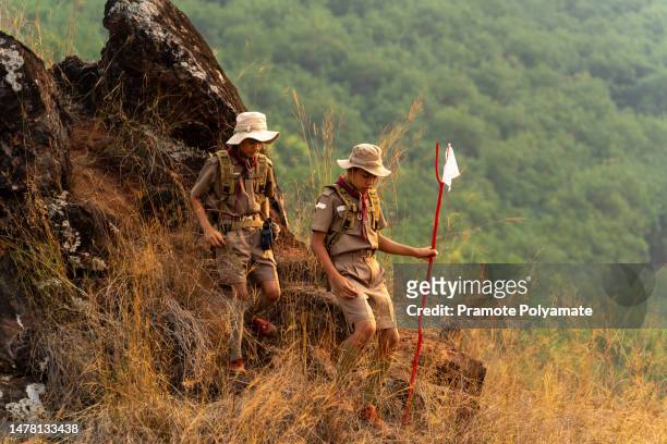 asian scout students, led by a squad leader and scouts in the squad, dressed in scout uniforms and backpacks, set off on a long journey in the mountain forests. concept of long distance training, discipline and patience of scout subjects. - indochina stock-fotos und bilder