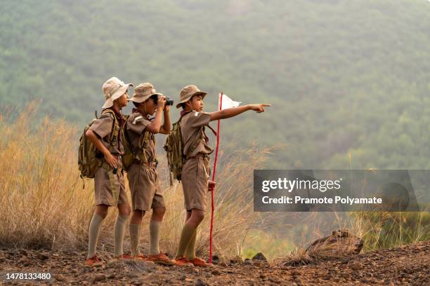 asian scout students, led by a squad leader and a group of scouts wearing scout uniforms are exploring nature with binoculars in a mountain camp. landscape survey concept. - indochina stock-fotos und bilder