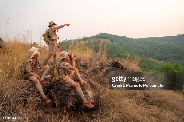 asian boy scout leader stands and points out the long-distance targets for the scouts in the team for the next day's journey near sunset. landscape survey concept. - scouts honour stock pictures, royalty-free photos & images