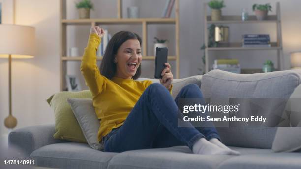 phone, happy and woman celebrating on a sofa, excited and cheerful for good news in her home. yes, success and online winner on smartphone app for message, promotion or email in a living room - achievement stock pictures, royalty-free photos & images