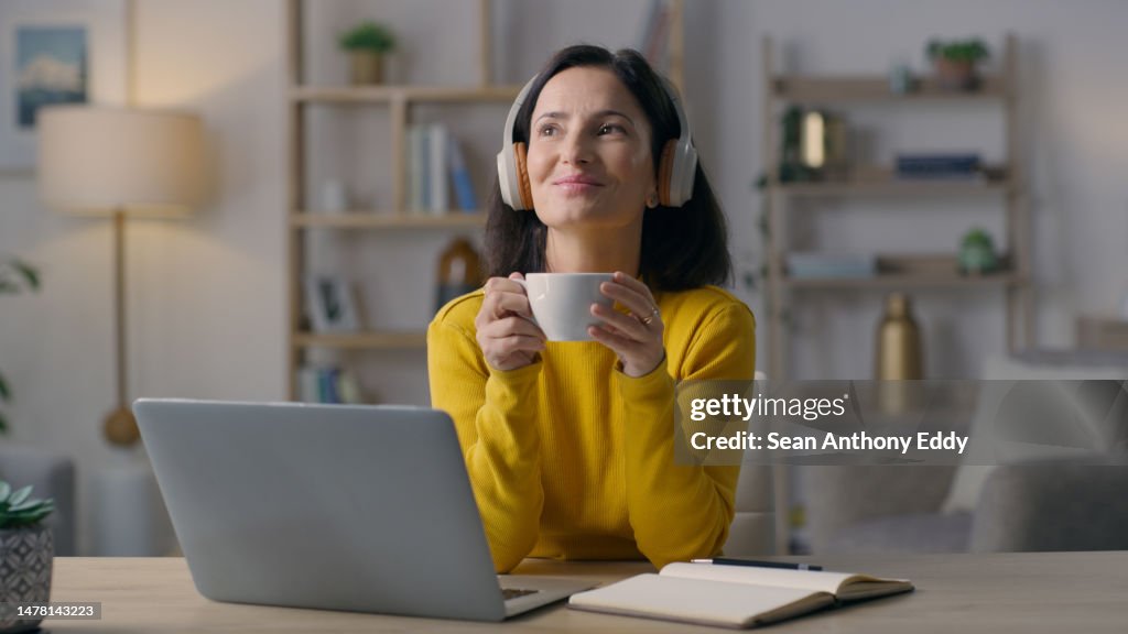 Woman with coffee, headphones and thinking with music remote work and freelance journalist with laptop. Working from home, female listen to podcast or radio, drink and think of content inspiration