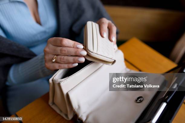 female hands of an unrecognizable person take out a wallet from  purse sitting at a table in a cafe for payment - multi colored purse stockfoto's en -beelden