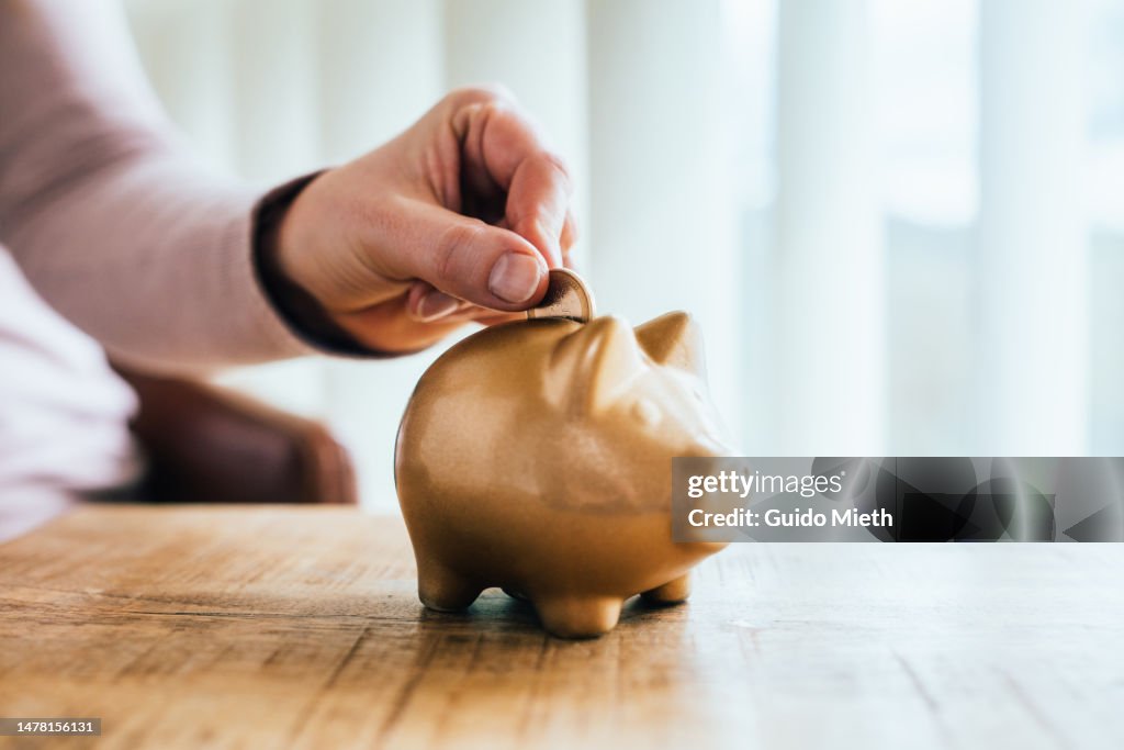 Woman putting a one euro coin in a golden piggy bank.