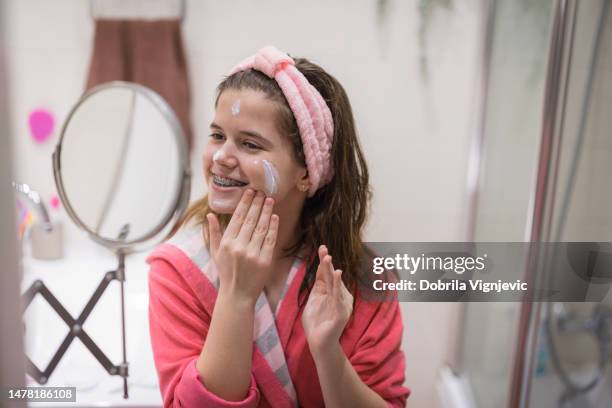 adolescente feliz aplicando crema facial hidratante - untar fotografías e imágenes de stock