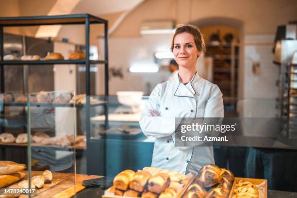 fröhliche kaukasische verkäuferin mit verschränkten armen in einer handwerklichen bäckerei - bäckerin stock-fotos und bilder