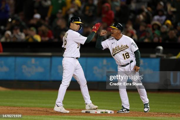 Aledmys Diaz of the Oakland Athletics is congratulated by first base coach Mike Aldrete after he hit a single that scored a run in the eighth inning...