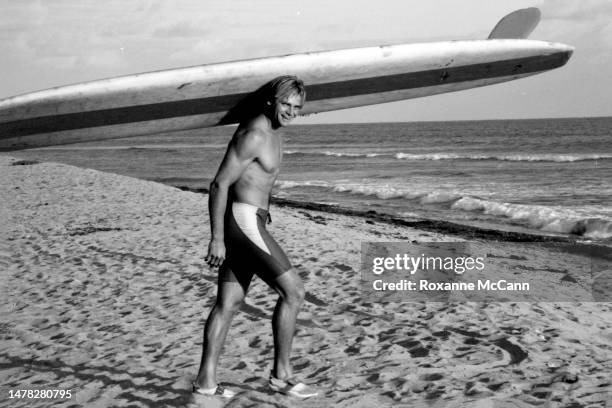 Surfer Laird Hamilton walks across Old Man's beach with his surfboard wearing Aqua Socks for a Nike commercial in 1990 in San Onofre, California.