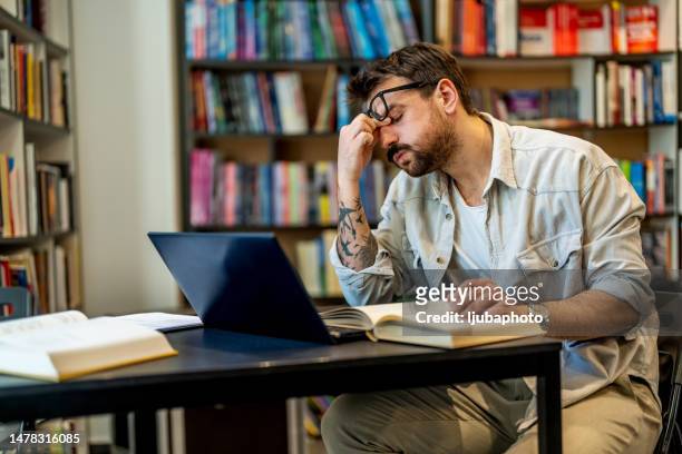 tired male adult student having too much to do in a library - arranjo imagens e fotografias de stock