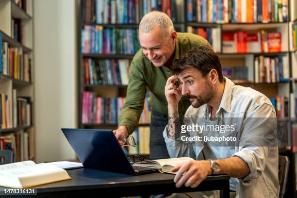male teacher helping adult student with studies in library - university student support stock pictures, royalty-free photos & images