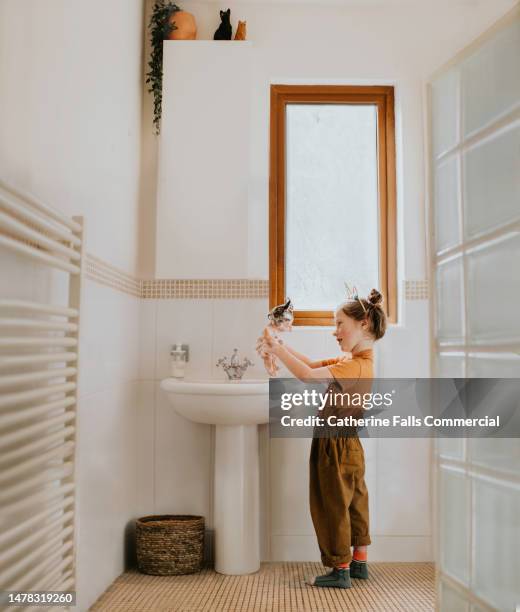 a young girl imitates real life, washing a rubber baby doll in a domestic sink in a bathroom - bath mat stockfoto's en -beelden