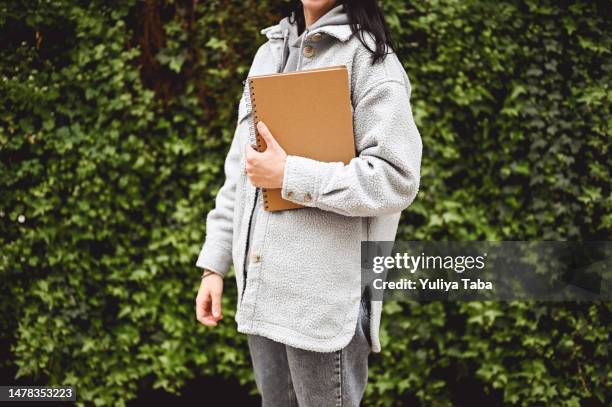 midsection of unrecognizable woman in a coat with a black note pad. - nature magazine stock pictures, royalty-free photos & images