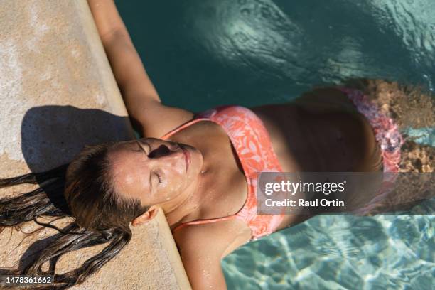 woman in bikini floating in a pool resort during summer holidays - mid volwassen vrouw stockfoto's en -beelden