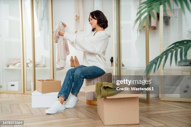 young woman choosing clothes to recycle at home - entrümpeln stock-fotos und bilder