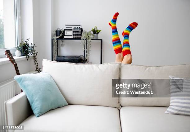 legs of mature woman wearing rainbow stockings behind sofa at home - legs in stockings stock pictures, royalty-free photos & images