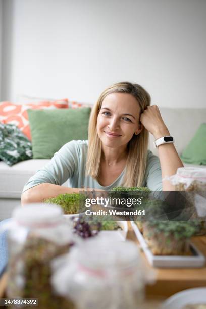 smiling mature woman sitting with homegrown herbs in living room - mature woman herbs stock pictures, royalty-free photos & images