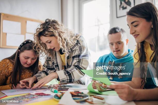 people with down syndrome and cerebral palsy doing an art project with help with assistants and animators.disability health care art workshop. - maatschappelijk werker stockfoto's en -beelden