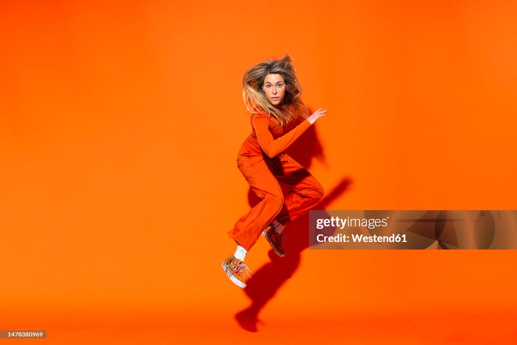 Active woman jumping against orange background