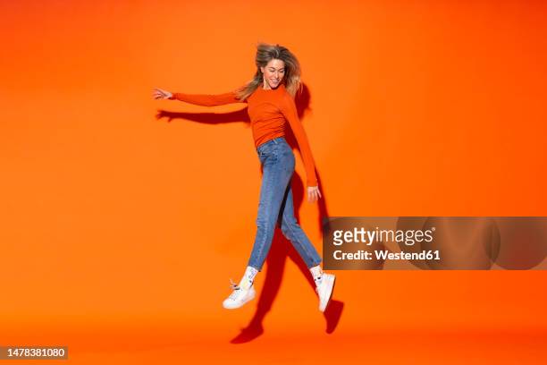 smiling woman levitating against orange background - levitación fotografías e imágenes de stock