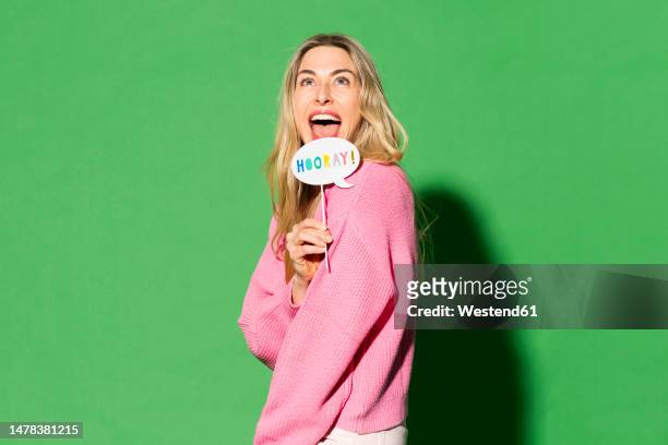 happy woman with speech bubble against green background - blonde cheering stock-fotos und bilder